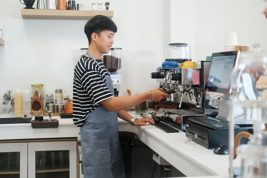 Young cheerful barista wearing apron while preparing coffee at an automatic machine in a modern coffee shop. photo