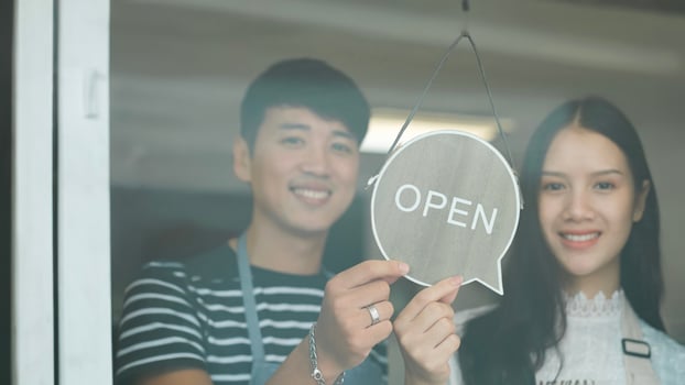 Happy Coffee Shop owner in an apron turning open sign board on glass door. Small business owner opening a small business. photo