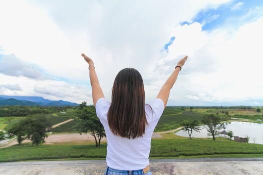 A young woman stands with her arms outstretched on a balcony above a beautiful tea plantation to symbolize her happiness in traveling and relaxing during the holidays. holiday happiness concept photo