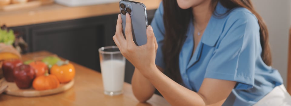 A young woman with a beautiful face in a blue shirt with long hair eating fruit sitting inside the kitchen at home with a laptop and notebook for relaxation, Concept Vacation. photo