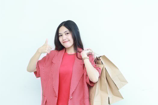 portrait of beautiful asian woman wearing red outfit gesturing carrying lots of shopping bags with happy expression photo