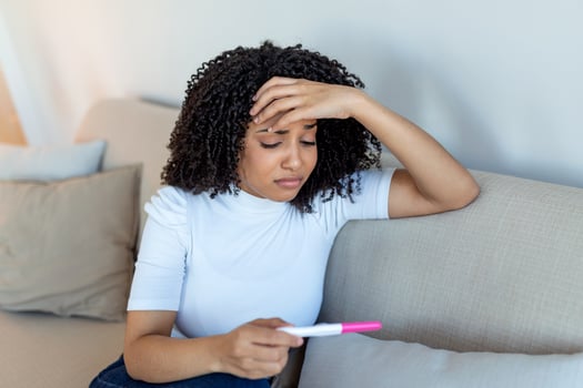 Sad, worried african american woman checking her recent pregnancy test, sitting on couch at home. Maternity, child birth and family problems concept. unwanted pregnancy photo