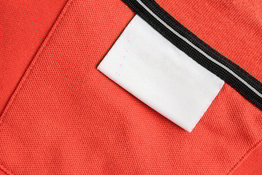 Blank white laundry care clothes label on orange shirt fabric texture background photo