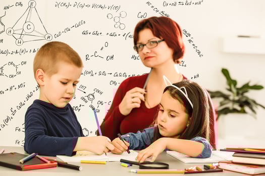 Female teacher helping children with homework in classroom at school photo