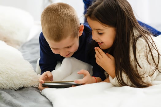 People, children, technology, friends and friendship concept - happy little girls boy with smartphones lying on floor at home photo