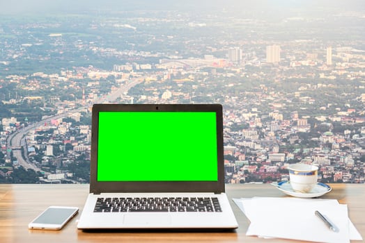 Mockup image of laptop with blank green screen,smartphone,coffee cup on wooden table view outdoors of office building dense cityscape high angle view background. photo