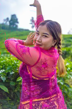an Asian woman in a pink costume is posing in front of a tea plantation photo