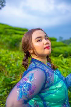 a beautiful Asian woman is posing in her blue dress in front of a park photo