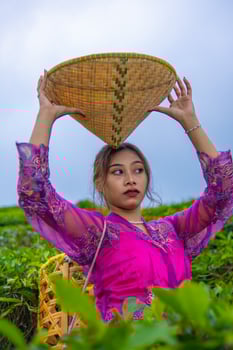 a tea garden farmer posing among the tea leaves while holding a hat and bamboo basket photo