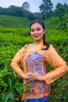 a tea leaf farmer in an orange dress posing in front of a very beautiful tea garden photo