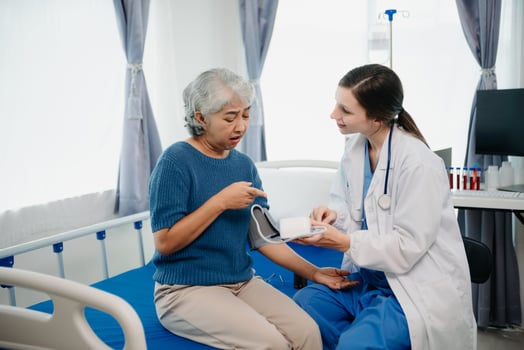Doctor in white suit take notes while discussing and Asian elderly, woman patient who lying on bed with receiving saline solution in hospital or clinic. photo