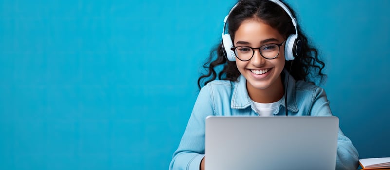 Smiling Indian teen girl using laptop for online study on blue background Happy student in educational webinar photo