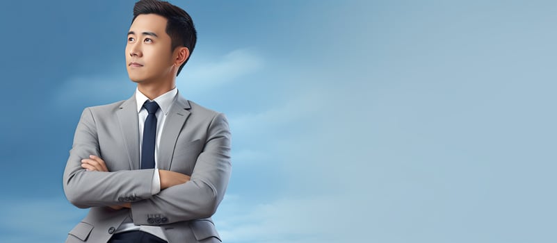 Portrait of attractive Southeast Asian businessman with crossed arms looking to side on blue background photo