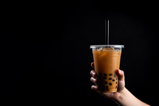 A hand holding takeaway plastic cup of delicious iced bubble milk tea and black pearls isolated on black background with copy space. ai generated photo