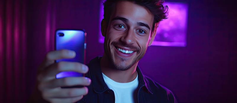 Man using smartphone for video call and taking selfies hipster lifestyle blogger portrait with purple background neon lights fashion trends room for text photo