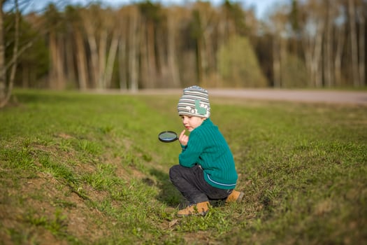 A funny boy walks through the spring park, examines the leaves with a large magnifying glass, looks for bugs and enjoys. photo