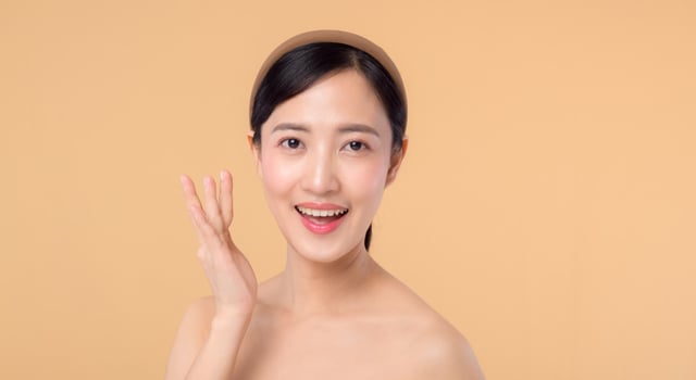 Beautiful girl asian model touching fresh glowing hydrated facial skin on beige background closeup. Beauty face young woman with natural makeup and healthy skin portrait. Skin care concept photo