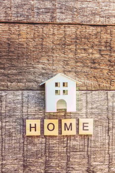 Miniature toy house with inscription HOME letters word on wooden background. Mortgage property insurance dream home concept. Flat lay top view, copy space photo