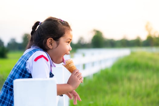 Cute Asian girl in school uniform eating ice cream while on vacation with family, and blured of green field rice  nature background, Happy family concept photo
