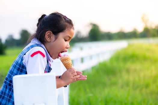 Cute Asian girl in school uniform eating ice cream while on vacation with family, and blured of green field rice  nature background, Happy family concept photo