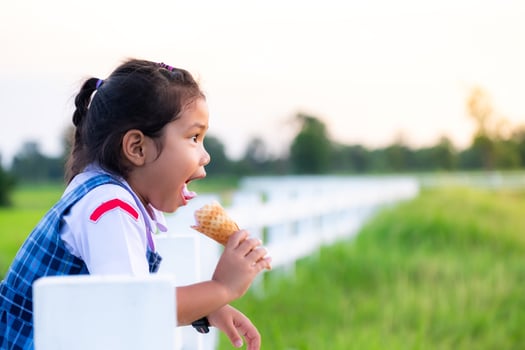 Cute Asian girl in school uniform eating ice cream while on vacation with family, and blured of green field rice  nature background, Happy family concept photo