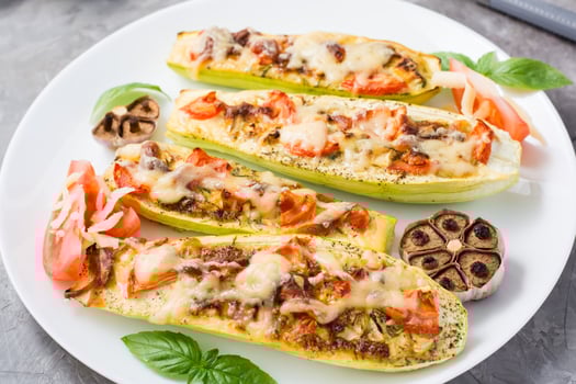 Ready-to-eat baked zucchini halves stuffed with cheese and tomato and basil leaves on a plate on the table. Vegetable dishes, healthy food. Close-up photo