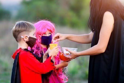 Children trick or treat in Halloween costume and medical mask. A boy and a girl in suits during the coronavirus pandemic receive candy from a woman . photo