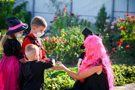Children trick or treat in Halloween costume and medical mask. A little boy, girl and baby in suits during the coronavirus pandemic receive candy from a woman. photo