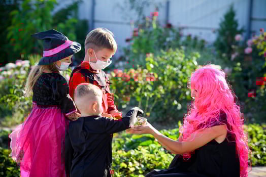 Children trick or treat in Halloween costume and medical mask. A little boy, girl and baby in suits during the coronavirus pandemic receive candy from a woman . photo