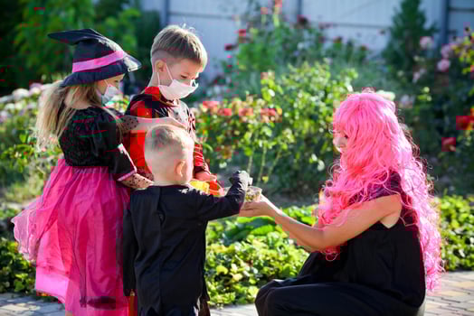 Children trick or treat in Halloween costume and medical mask. A boy and a girl in suits during the coronavirus pandemic receive candy from a woman . photo
