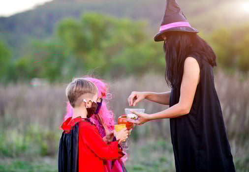 Children trick or treat in Halloween costume and medical mask. A boy and a girl in suits during the coronavirus pandemic receive candy from a woman. photo