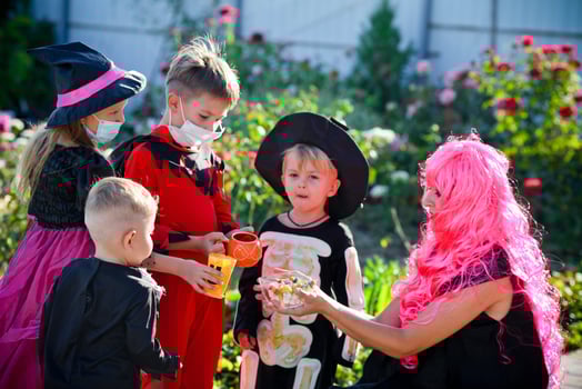 Children trick or treat in Halloween costume and medical mask. A little boy, girl and baby in suits during the coronavirus pandemic receive candy from a woman . photo