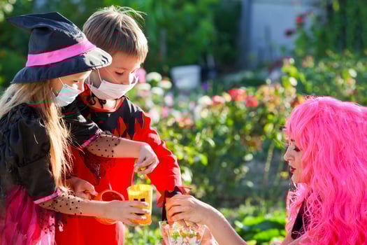 Children trick or treat in Halloween costume and medical mask. A little boy and a girl in suits during the coronavirus pandemic receive candy from a woman dressed. photo