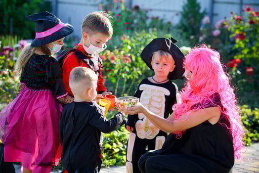 Children trick or treat in Halloween costume and medical mask. A little boy, girl and baby in suits during the coronavirus pandemic receive candy from a woman. photo