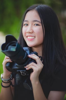 asian teenager toothy smiling face and holding dslr camera in hand photo