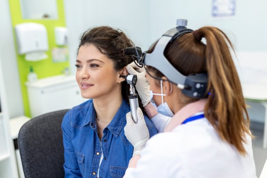 Hearing exam. Otolaryngologist doctor checking woman's ear using otoscope or auriscope at medical clinic. Otorhinolaryngologist pulling ear with hand and looking at it with otoscope closeup. photo