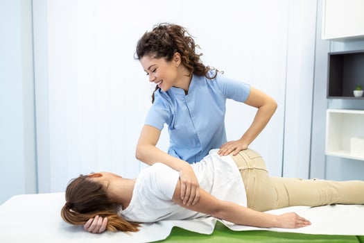 Young woman doctor chiropractor or osteopath fixing lying womans back with hands movements during visit in manual therapy clinic. Professional chiropractor during work photo