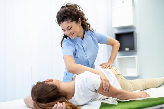 Young doctor chiropractor or osteopath fixing lying womans back with hands movements during visit in manual therapy clinic. Professional chiropractor during work photo