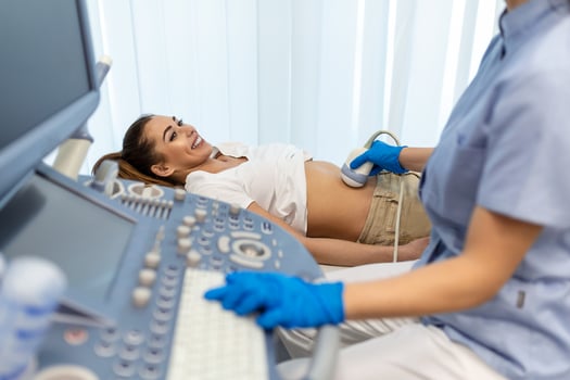 Side view portraits of gynecologist in white lab coat and sterile gloves using ultrasound scanner while examining female patient. woman lying on daybed on blurred background photo