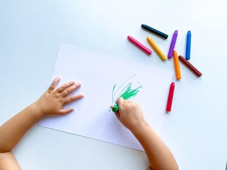 small child draws with pastel crayons on white table. photo