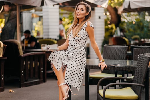 beautiful smiling woman dressed in white printed dress in street cafe photo