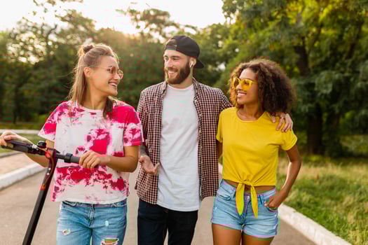 happy young company of smiling friends walking in park with electric kick scooter photo