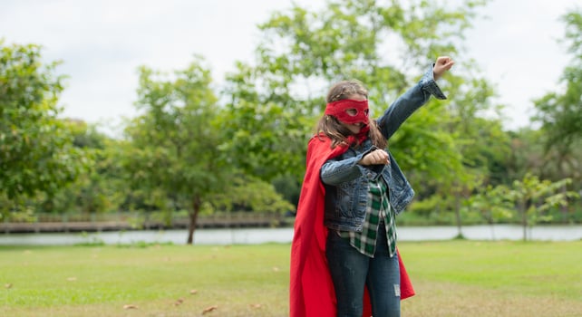 On a beautiful day in the park, a young girl enjoys her vacation. Playful with a red superhero costume and mask. photo