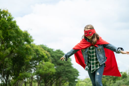 On a beautiful day in the park, a young girl enjoys her vacation. Playful with a red superhero costume and mask. photo