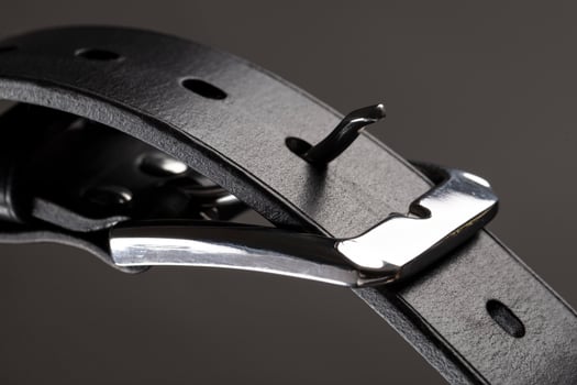 Part of a black leather belt with a metal buckle close-up on a gray background. photo