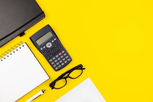 Modern office desk flat lay with spiral paper notepad, white envelopes mockup and reading glasses on yellow background. Top view. Copy space. photo