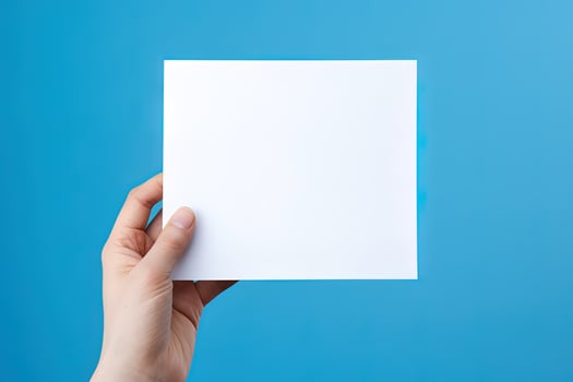 A human hand holding a blank sheet of white paper or card isolated on blue background. ai generated photo