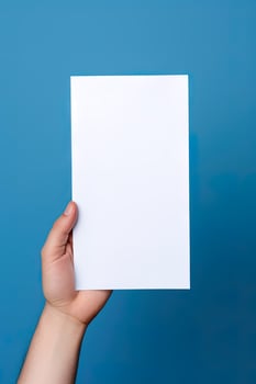 A human hand holding a blank sheet of white paper or card isolated on blue background. ai generated photo