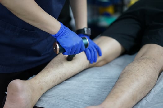 Muscle massage after a hard workout. Physical therapist treats injury of male patient athlete leg. Massage Gun Machine Recovery Therapy And Stimulation photo