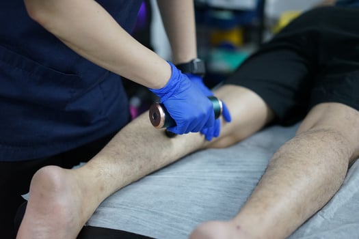 Muscle massage after a hard workout. Physical therapist treats injury of male patient athlete leg. Massage Gun Machine Recovery Therapy And Stimulation photo